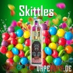 Randm Tornado 7000 vape ile Skittles şekerinin canlı bir karışımı, renkli küreler ve yeşil bir zemin sergiliyor.